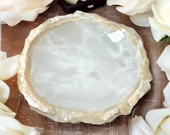 May include: A white and beige decorative tray with a natural, organic edge. The tray is surrounded by white roses and petals. The tray is likely made of stone or a similar material, and is suitable for displaying jewelry or small items.