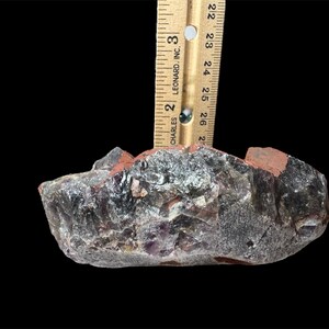 May include: A large, rough amethyst crystal with a purple and gray color. The crystal is approximately 2.5 inches wide and has a natural, irregular shape.
