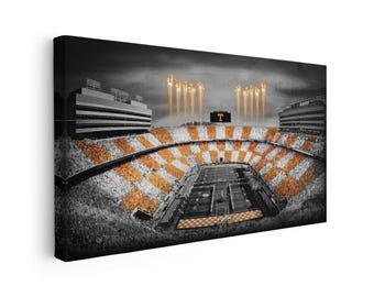 Puede incluir: Un lienzo panorámico de un estadio de fútbol en blanco y negro con coloración naranja selectiva en las secciones de asientos y el campo. Fuegos artificiales se elevan sobre el estadio y un marcador muestra una gran letra T naranja al centro.