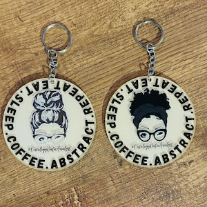 May include: Two round keychains with black and white illustrations of a woman with glasses and a bun. The text on the keychains reads "COFFEE.SLEEP.EAT.REPEAT" and "#OncologyDataAnalyst".