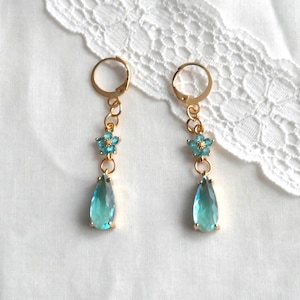 May include: Gold dangle earrings with a teardrop shaped blue gemstone and a small blue flower charm.
