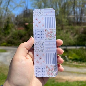 May include: A bookmark with a patchwork design featuring floral patterns in shades of pink and blue on a white background.