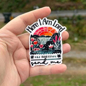 May include: A sticker with the text "Here I Am Lord" above a landscape scene with a sunset, flowers, and the text "send me." The sticker also includes the text "Isaiah 6:8."