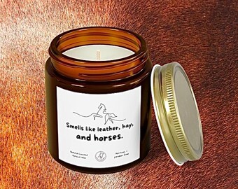 May include: A brown glass jar candle with a gold lid, labeled "Smells like leather, hay, and horses." The candle has a white label with a horse illustration. The candle is made with natural coconut and apricot wax.