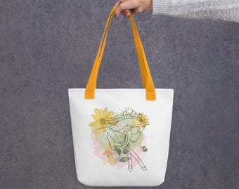 May include: White tote bag with yellow handles, featuring a line drawing of a horse with floral accents in yellow, green, and pink. The design includes sunflowers and a bee. The bag is held by a person.