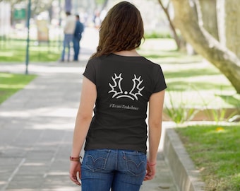 May include: Black t-shirt with a white graphic design on the back, featuring a stylized crown and antlers, with the text "#TeamTrakeliner" below. The person is wearing blue jeans and walking on a paved path.