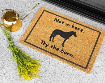 May include: A rectangular doormat with a black border and the text "Not in here. Try the barn." features a black horse silhouette. A gold watering can and a bundle of yellow flowers are also in the image.