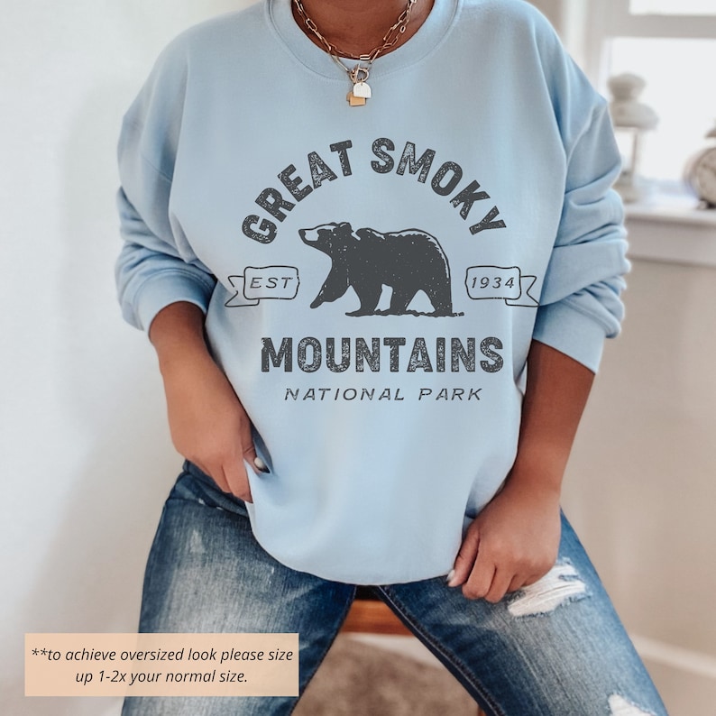 May include: Light blue sweatshirt with a graphic of a bear and the text "Great Smoky Mountains National Park" in black. The text "Est 1934" is also included in the graphic.