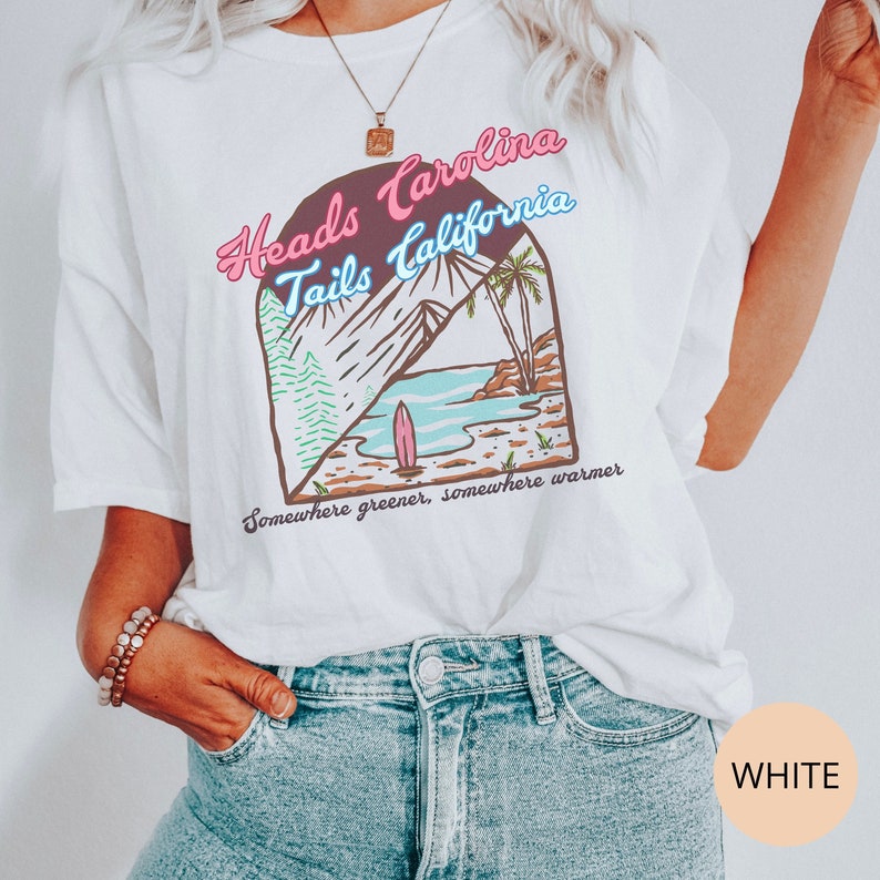 May include: White t-shirt with a graphic print of a beach scene and the text "Heads Carolina Tails California" and "Somewhere greener, somewhere warmer".