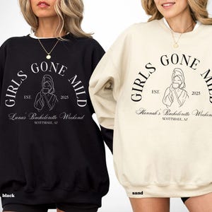 May include: Black and sand-colored sweatshirts with the text "GIRLS GONE MILD" in a semi-circular design. The sweatshirts also feature the text "Lana's Bachelorette Weekend" and "Hannah's Bachelorette Weekend" with the year "2025" and the city "Scottsdale, AZ".