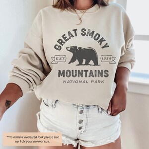 May include: A cream colored sweatshirt with the text "Great Smoky Mountains National Park" in black. The text is surrounded by a black bear graphic and a banner with the text "Est. 1934".