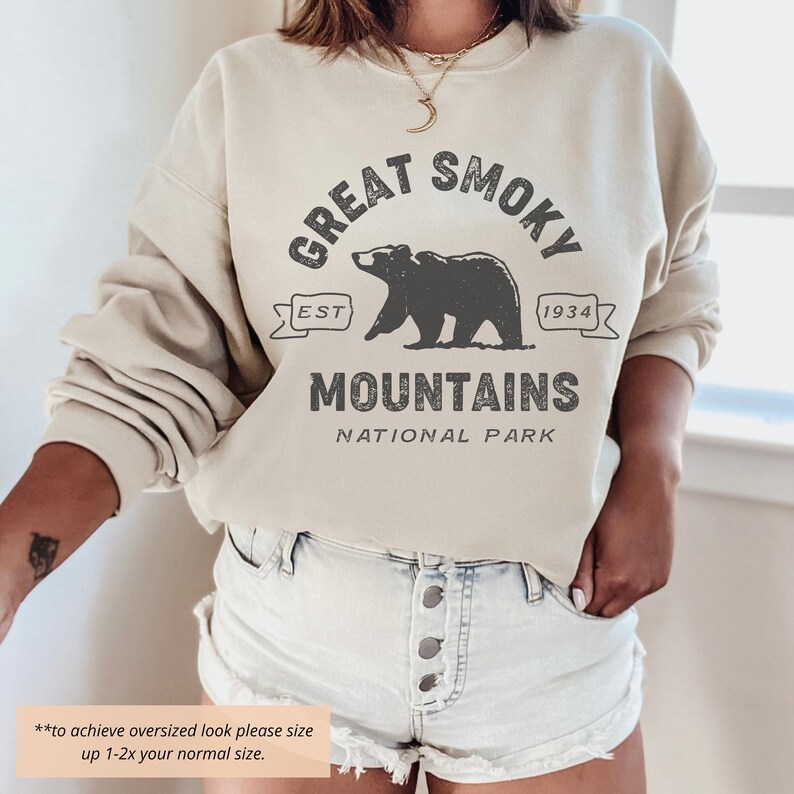 May include: A cream colored sweatshirt with the text "Great Smoky Mountains National Park" in black. The text is surrounded by a black bear graphic and a banner with the text "Est. 1934".