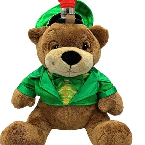 May include: A brown teddy bear wearing a green jacket and a green hat with a red funnel on top. The bear is sitting with its legs crossed and has a green bow tie.