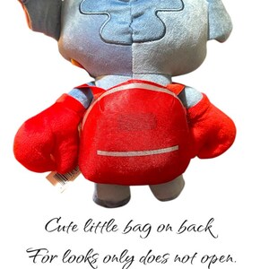 May include: A plush toy of a blue and gray alien character with large red hands and a red backpack. The text on the image says, "Cute little bag on back. For looks only does not open."