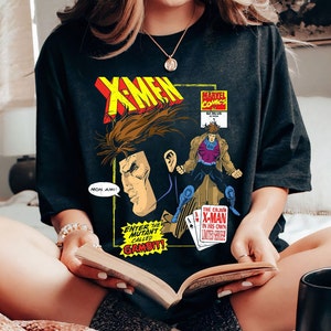 Pode incluir: Uma camiseta preta com um gráfico de banda desenhada com Gambit dos X-Men. O gráfico está em um estilo vintage com um esquema de cores vermelho, amarelo e azul. O texto no gráfico diz "Enter the Mutant Called Gambit!" e "The Cajun X-Man in His Own Limited Series!"