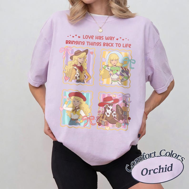 May include: A light purple t-shirt featuring four rectangular panels with cartoon illustrations of characters and a cowboy boot. The text reads, Love has way BRINGING THINGS BACK TO LIFE. The design includes pink bows, hearts, and colorful blocks.