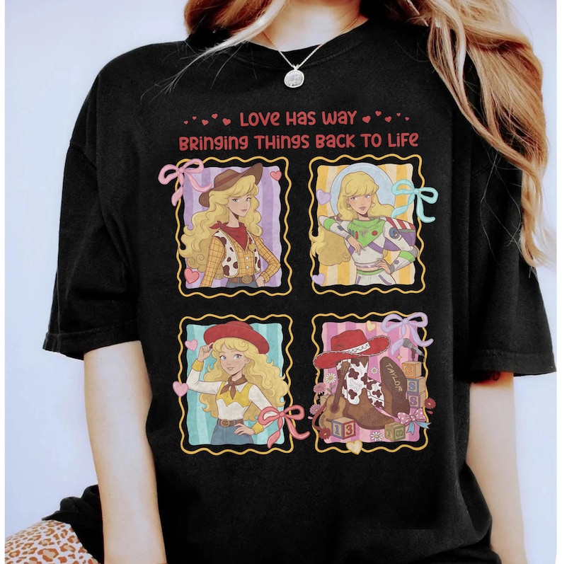 May include: A black t-shirt featuring a graphic print with the text "LOVE HAS WAY BRINGING THINGS BACK TO LIFE". The design includes four square panels showing a blonde character dressed as a cowgirl, a space ranger, and a cowgirl with boots.