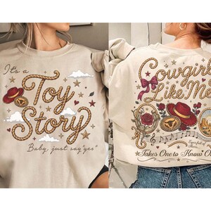 Pu&ograve; includere: Una felpa beige con due disegni. Il davanti mostra una scritta in stile corda che recita It's a Toy Story Baby, just say yes con un cappello rosso e nuvole. Il retro mostra Cowgirl Like Me con un cappello rosso, rose, un ferro di cavallo e note.