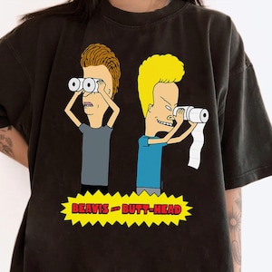 May include: Dark grey t-shirt with a cartoon graphic of Beavis and Butt-Head. Beavis is using binoculars, and Butt-Head is using toilet paper as a telescope. The text "BEAVIS AND BUTT-HEAD" is in a yellow banner.