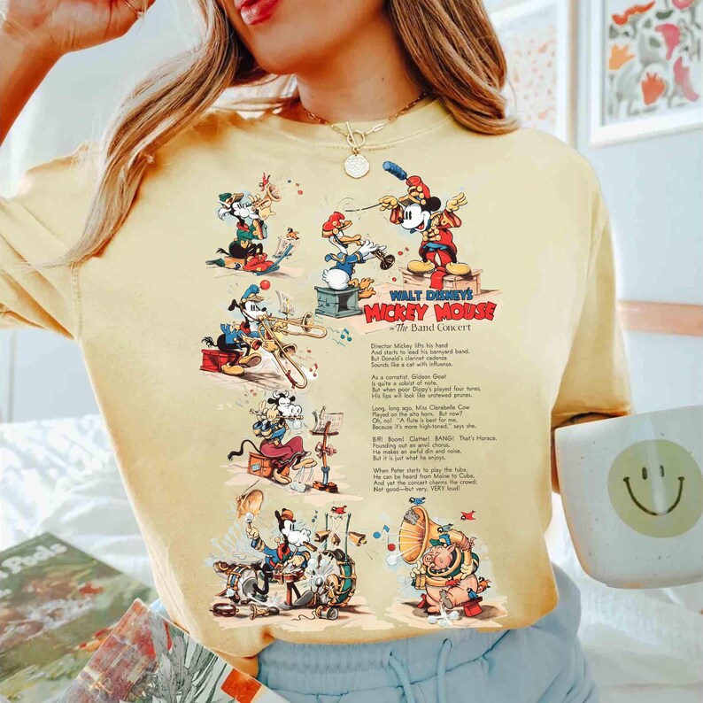 Puede incluir: Camiseta amarilla clara con un dise&ntilde;o vintage del concierto de la banda Mickey Mouse de Walt Disney. El gr&aacute;fico incluye a Mickey Mouse, el Pato Donald y Goofy tocando instrumentos. El texto de la camiseta dice "Mickey Mouse The Band Concert".