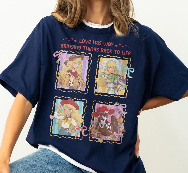 May include: A navy blue t-shirt featuring the text "LOVE HAS WAY BRINGING THINGS BACK TO LIFE" in pink. The graphic includes four framed illustrations of a blonde character in various outfits, including a cowgirl, a space ranger, and a cowboy boot.