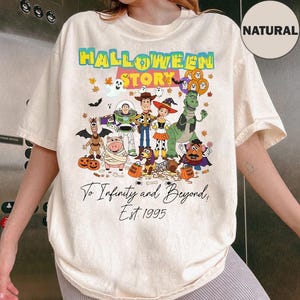 Puede incluir: Camiseta color crema con un gráfico colorido de personajes de Toy Story disfrazados para Halloween. El texto "HALLOWEEN STORY" está en la parte superior, con "To Infinity and Beyond, Est. 1995" debajo. La camiseta tiene mangas cortas y un corte holgado.