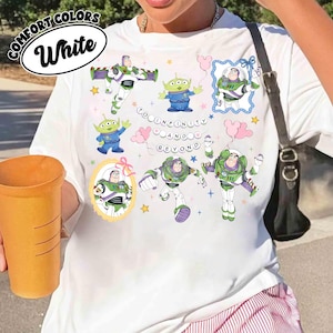 Puede incluir: Camiseta blanca con im&aacute;genes de dibujos animados de Buzz Lightyear y Little Green Men, con la frase "TO INFINITY AND BEYOND". La camiseta tiene una etiqueta Comfort Colors.