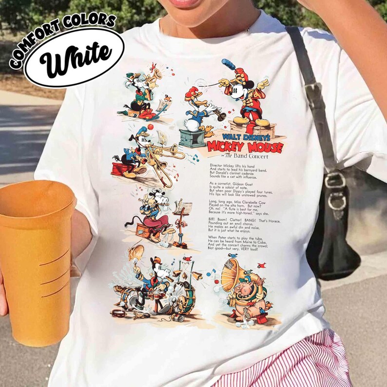 Puede incluir: Camiseta blanca con un gr&aacute;fico de dibujos animados vintage de Mickey Mouse dirigiendo una banda. El gr&aacute;fico incluye varios personajes de Disney tocando instrumentos, con el texto "WALT DISNEY'S MICKEY MOUSE - The Band Concert."