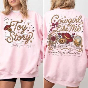 Pu&ograve; includere: Una felpa girocollo rosa chiaro con una stampa grafica sul davanti e sul retro. Il davanti mostra il testo It's a Toy Story Baby, just say yes con un carattere a corda, un cappello rosso e stelle. Il retro mostra Cowgirl Like Me con un cappello rosso, rose, un ferro di cavallo e note musicali.