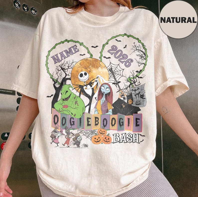 May include: A natural-coloured t-shirt featuring a graphic print of characters from The Nightmare Before Christmas, including Jack Skellington, Sally, and Oogie Boogie. The design includes the text NAME, 2026, OOGIE BOOGIE BASH, and pumpkins.