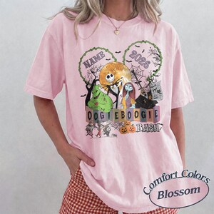 May include: A light pink t-shirt featuring a graphic print of characters from The Nightmare Before Christmas, including Jack Skellington, Sally, and Oogie Boogie, with the text NAME, 2026, and OOGIE BOOGIE BASH, surrounded by pumpkins and bats.