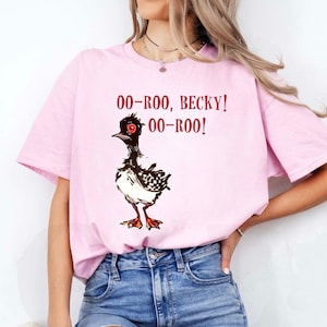 May include: A light pink t-shirt featuring a cartoon bird illustration with the text "OO-ROO, BECKY! OO-ROO!" in red. The bird is black, white, and red, with a checkered pattern on its chest.