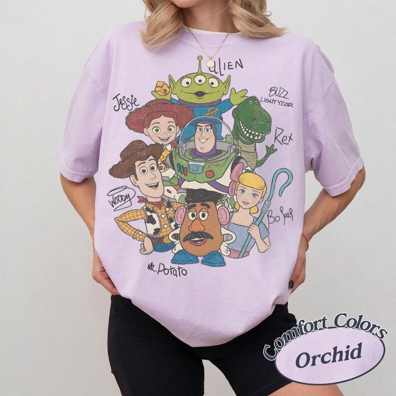 May include: Orchid-colored t-shirt featuring a graphic of Toy Story characters, including Woody, Buzz Lightyear, and Mr. Potato Head. The shirt has a Comfort Colors label.