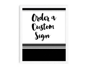 May include: A framed sign with the text "Order a Custom Sign" in black script. The sign has a white background with a black border at the top and bottom, and a solid black section at the bottom.