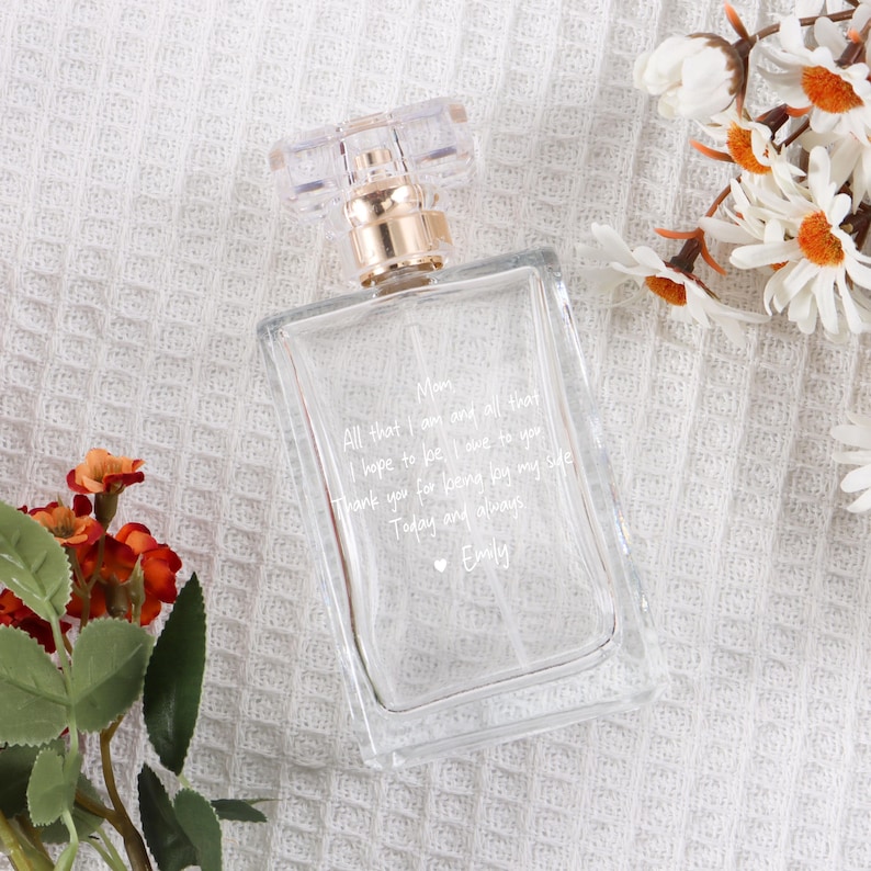 May include: A clear glass perfume bottle with a gold cap and a handwritten message on the bottle that reads: "Mom, All that I am and all that I hope to be I owe to you. Thank you for being by my side Today and always. Emily"