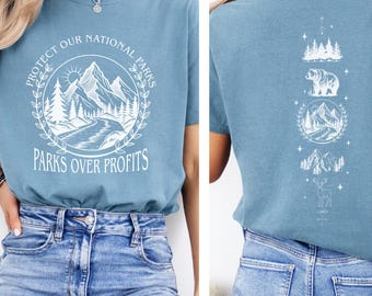 May include: A light blue t-shirt with a white graphic on the front that says "Protect Our National Parks" and "Parks Over Profits". The back of the shirt has a white graphic of a bear, mountains, and trees.