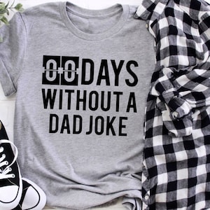 May include: A gray t-shirt with black text that reads "00 DAYS WITHOUT A DAD JOKE".