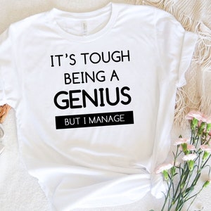 Puede incluir: Camiseta blanca con texto negro que dice "Es difícil ser un genio, pero lo consigo".