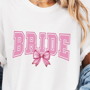 May include: White t-shirt with the word "BRIDE" in pink letters with a pink bow underneath.