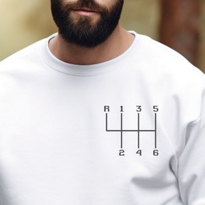 May include: White sweatshirt with a black graphic of a car's gear shift pattern. The pattern includes the letters R, 1, 2, 3, 4, 5, and 6.