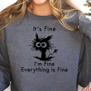 Może przedstawiać: Szara bluza z nadrukiem czarnego kota i tekstem "It's Fine I'm Fine Everything is Fine".