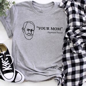 May include: A grey t-shirt with a black outline of a man's face and the text "YOUR MOM" -Sigmund Freud.