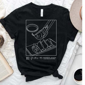 May include: Black t-shirt featuring a white graphic of Japanese gyoza dumplings. The text "餃子 (ギョーザ) JAPANESE GYOZA - CRAVINGS SATISFIED -" is printed below the graphic.