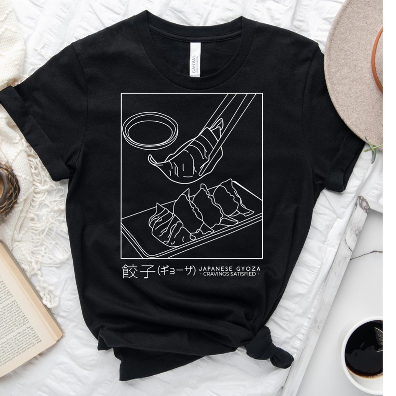 May include: Black t-shirt featuring a white graphic of Japanese gyoza dumplings. The text "餃子 (ギョーザ) JAPANESE GYOZA - CRAVINGS SATISFIED -" is printed below the graphic.
