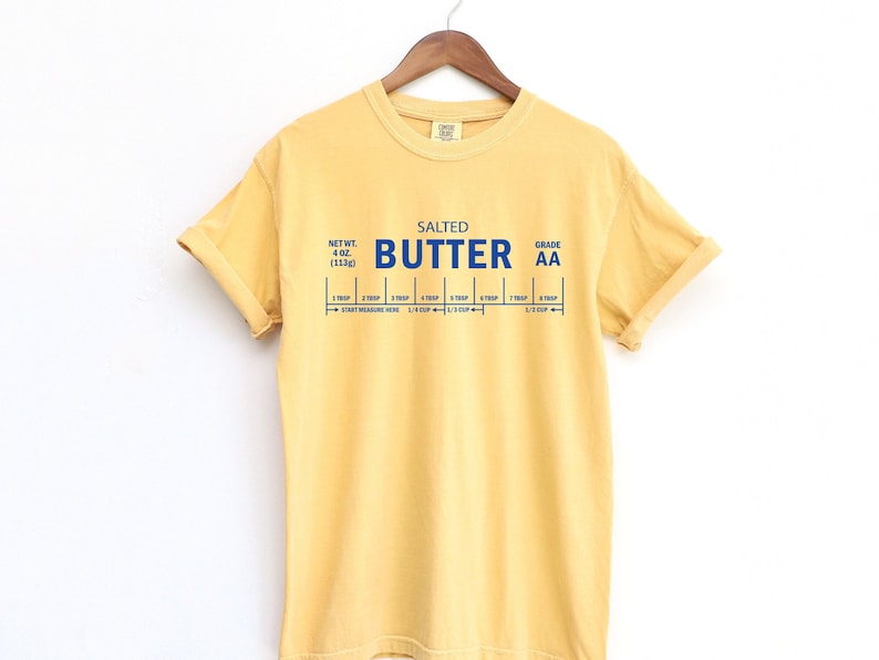 May include: A yellow t-shirt with a blue graphic of a stick of butter with the text "SALTED BUTTER GRADE AA" and a measurement guide for 4 oz (113g) of butter.