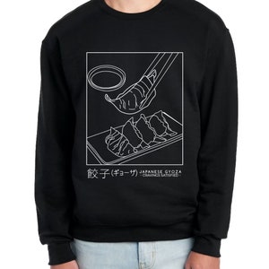 May include: Black sweatshirt featuring a white graphic of Japanese gyoza dumplings being lifted with chopsticks. The text "餃子 (ギョーザ) JAPANESE GYOZA -CRAVINGS SATISFIED- " is below the graphic.