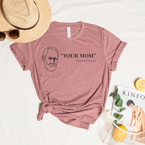 May include: A pink t-shirt with a black line drawing of Sigmund Freud and the text "YOUR MOM" - Sigmund Freud.