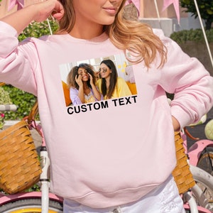 Op de afbeelding: Roze sweatshirt met een foto van twee lachende vrouwen en de tekst "CUSTOM TEXT" gedrukt op de voorkant.