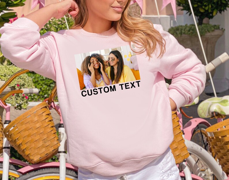 Op de afbeelding: Roze sweatshirt met een foto van twee lachende vrouwen en de tekst "CUSTOM TEXT" gedrukt op de voorkant.