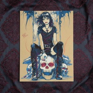 May include: Illustration of a woman with black hair and dark clothing seated on a skull. The artwork features a gothic aesthetic with blue and red accents. The woman wears a necklace with an ankh pendant and black boots. The background is a neutral tan colour.